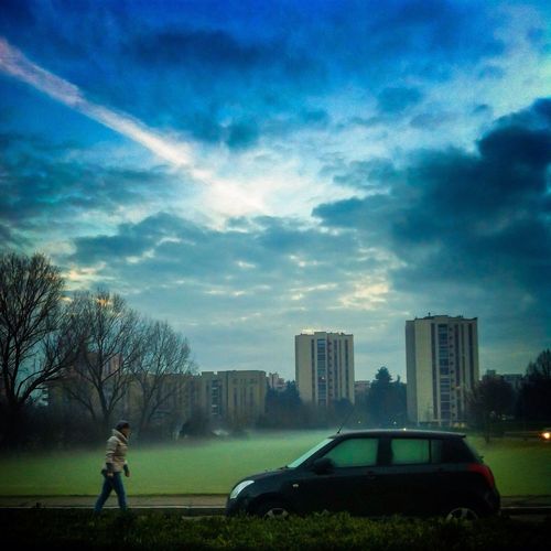 People walking on city street against cloudy sky