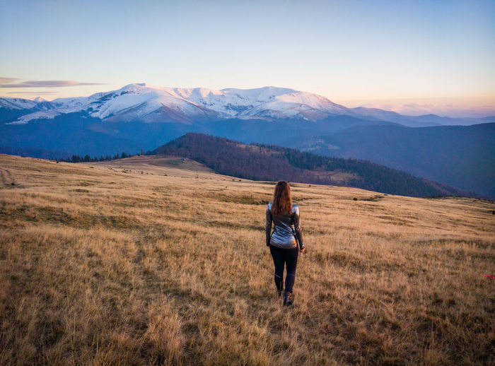 Rear view of woman walking on grassy mountain during sunset