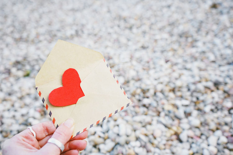 Cropped hand holding envelope with heart shape on pebbles
