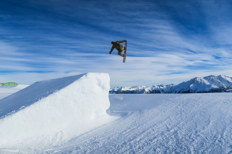 Person with snow board jumping over snow covered field against sky