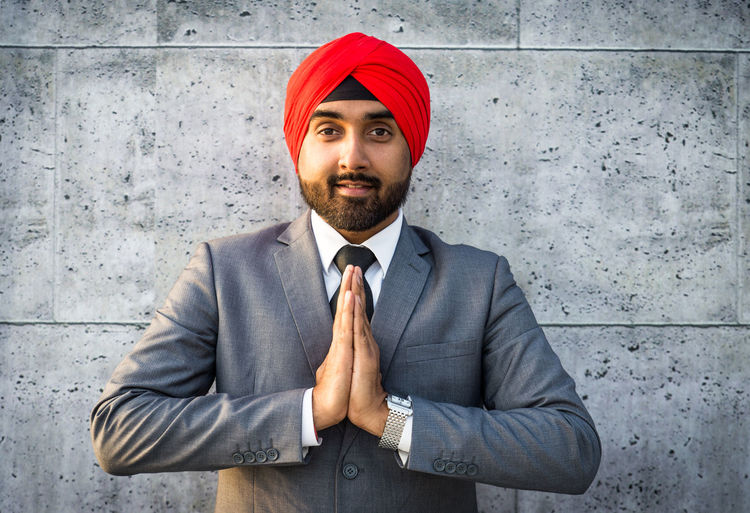 Portrait of smiling businessman wearing turban with clasped hands against wall