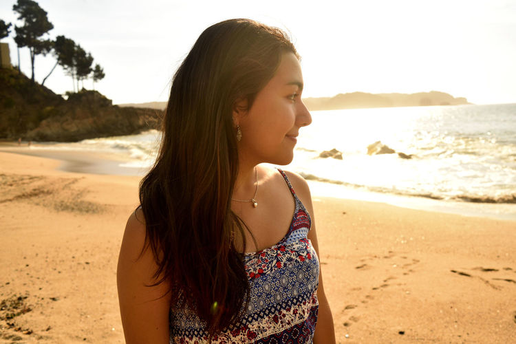 Young woman looking away while standing at beach against sky