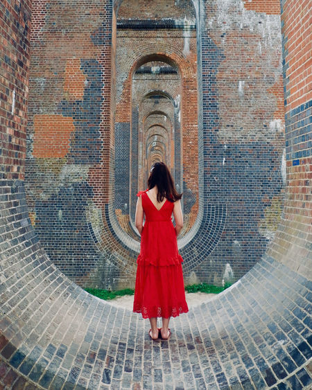 REAR VIEW OF WOMAN STANDING AGAINST RED BRICK WALL
