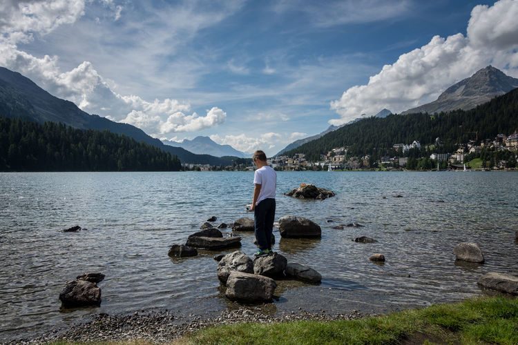 Rear view of boy standing on rock in lake against sky