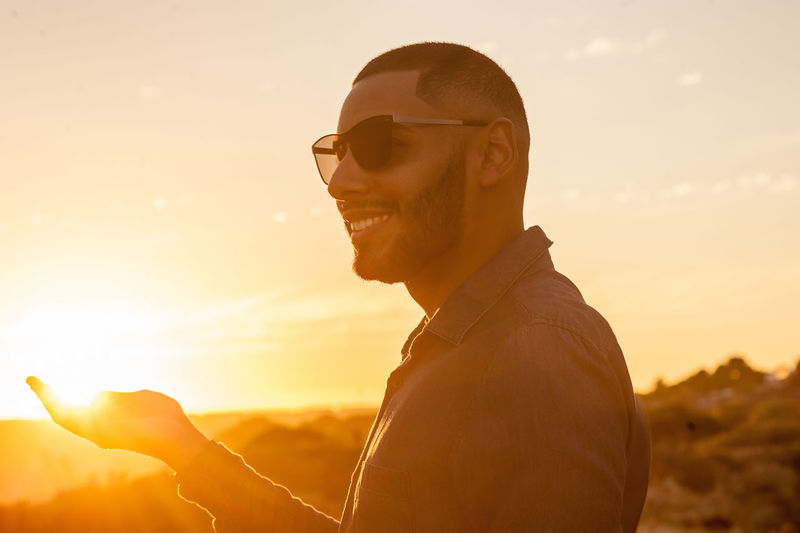 Portrait of young man using smart phone against sky during sunset
