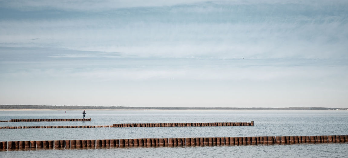 Wooden posts in sea against sky