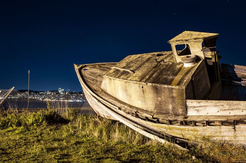 Abandoned boat on field against sky at night