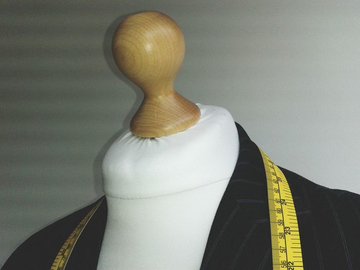 Jacket and measuring tape on dressmakers model against white wall