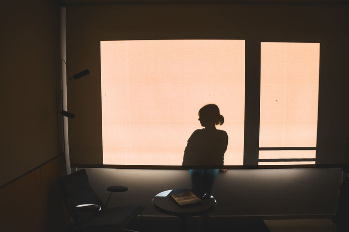 REAR VIEW OF SILHOUETTE WOMAN STANDING BY WINDOW