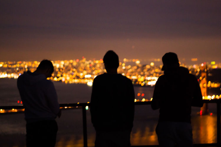 Silhouette people standing by railing against illuminated cityscape at night