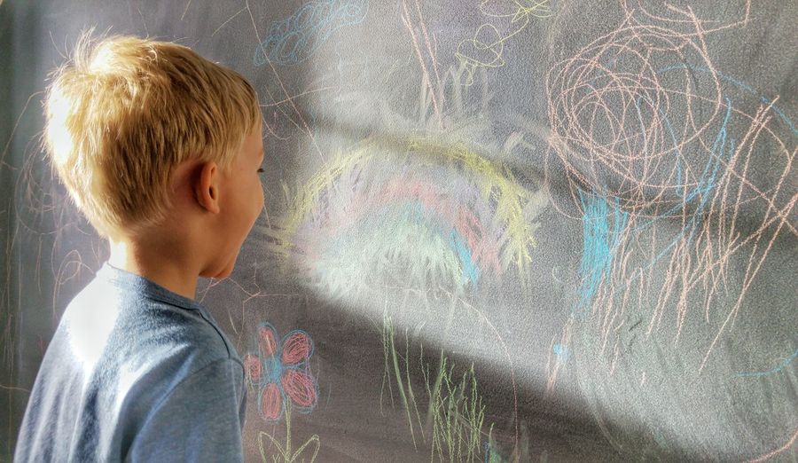 Close-up of child laughing in front of scribbles on chalkboard
