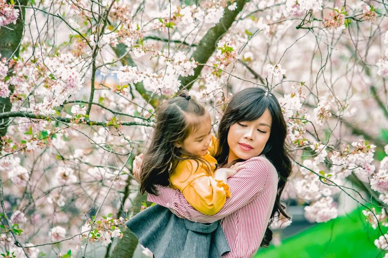 Beautiful young woman carrying daughter by cherry tree