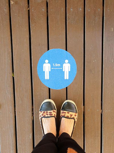 Low section of person standing over social distancing sign on wooden floor