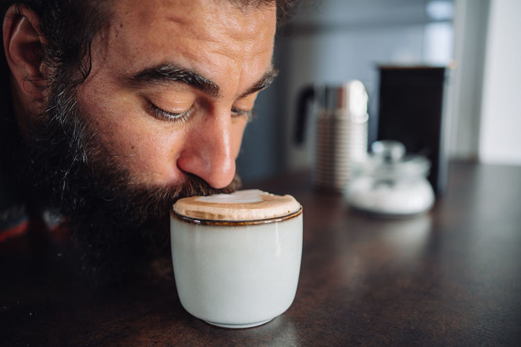 Detail of a bearded man drinking from a coffee cup with some milk foam