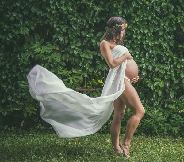 Full length of pregnant woman standing on grass against plants