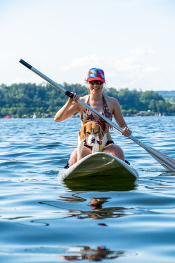 Adult woman on paddle board with male beagle, wallersee, austria.