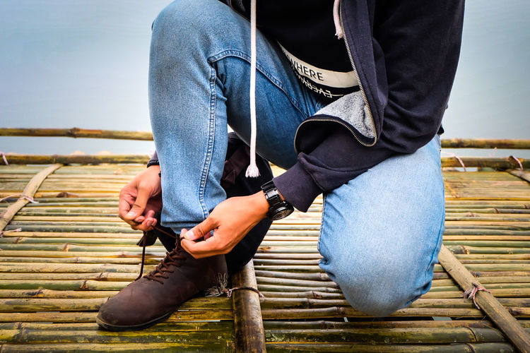 Low section of man tying shoelace on bamboo floor