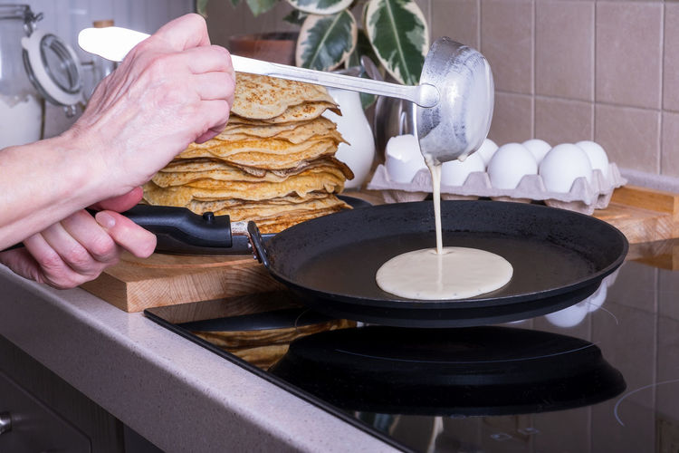 Housewife woman bakes pancakes for breakfast and pours dough into hot frying pan. 