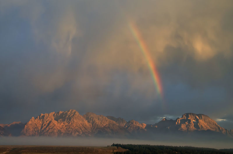 Scenic view of rainbow over mountains against sky during sunset