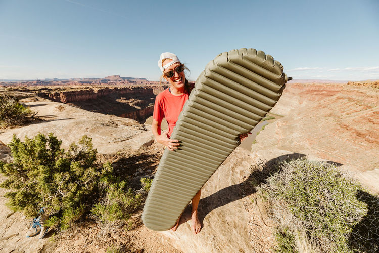 Female camper holding sleeping pad at campsite above grand canyon