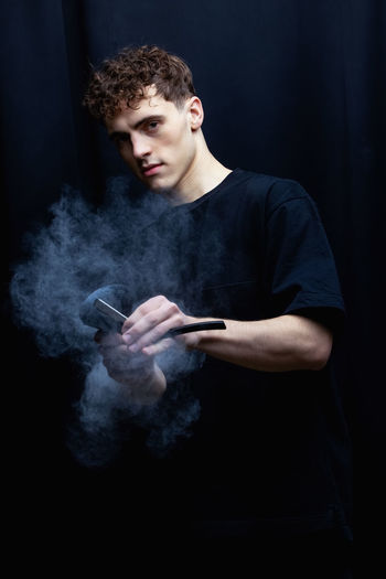 Portrait of young man holding razor against black background