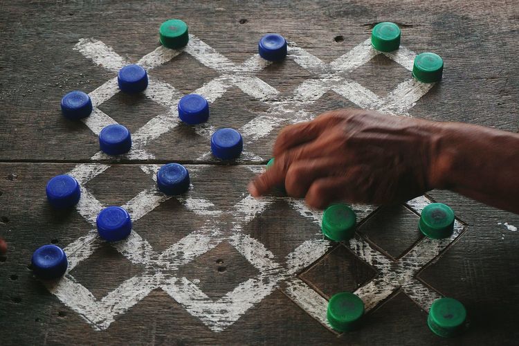 Man playing game of checkers on wooden board using bottle caps 
