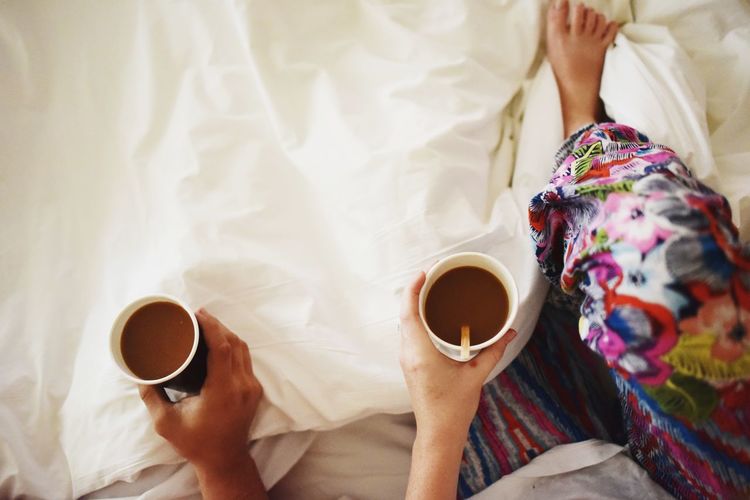 Low section of couple holding coffee cup on bed
