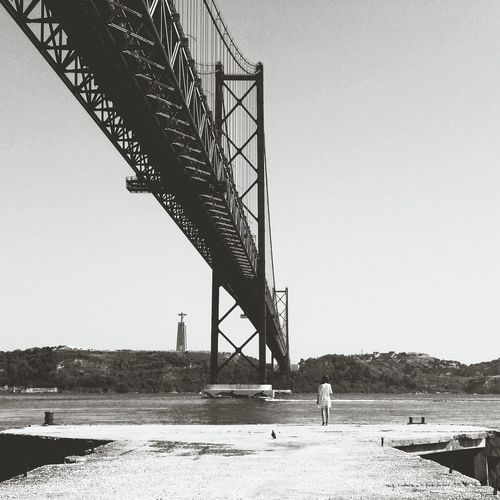 Rear view of woman standing by april 25th bridge and tagus river against sky