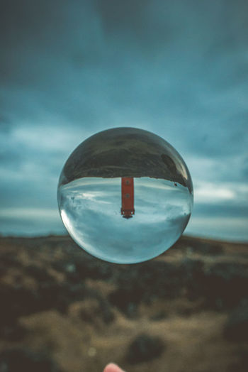 Close-up of crystal ball on landscape against sky