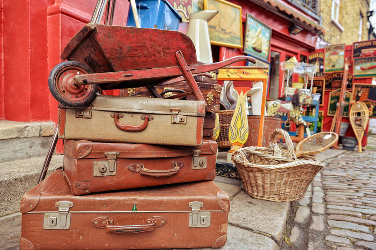 Stack of old travel trunks and wheelbarrow for sale on street