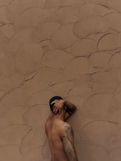 Shirtless tattooed man standing against wall
