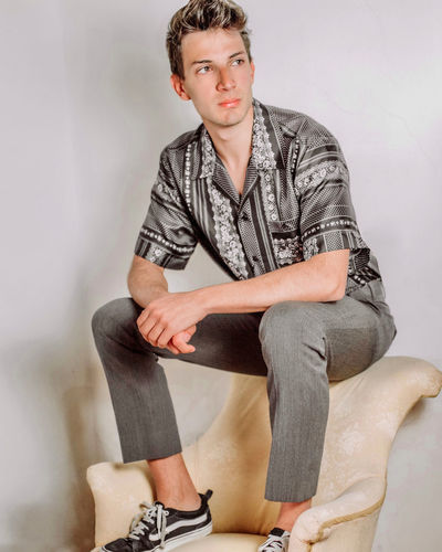 Portrait of young man sitting against wall
