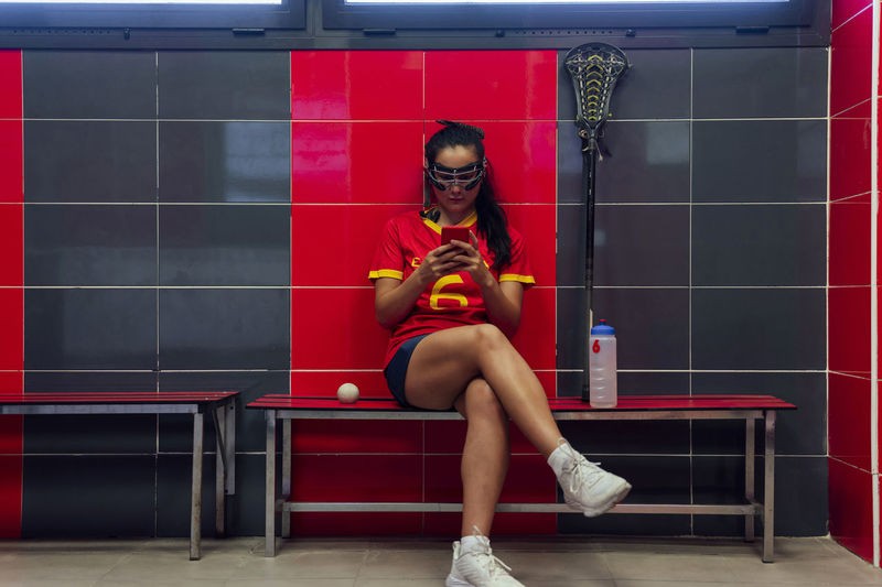 Player using smart phone sitting in lacrosse locker room