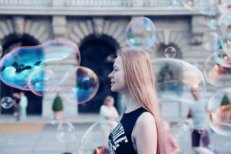 Side view of young woman standing amidst bubbles in mid-air