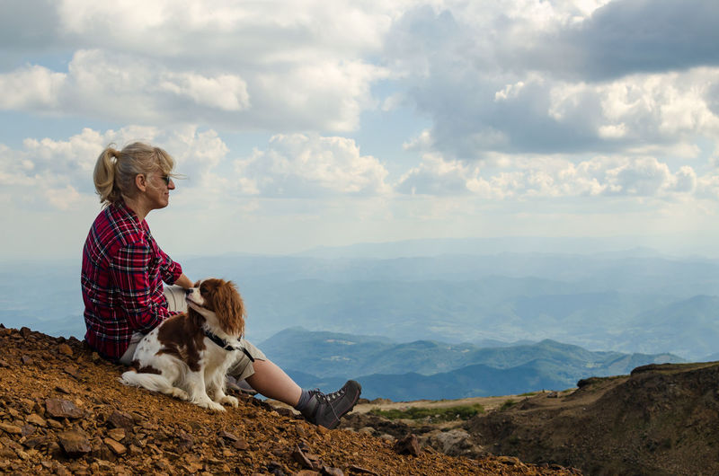 Woman and her dog, cavalier king charles spaniel, are watching picturesque mountain landscape