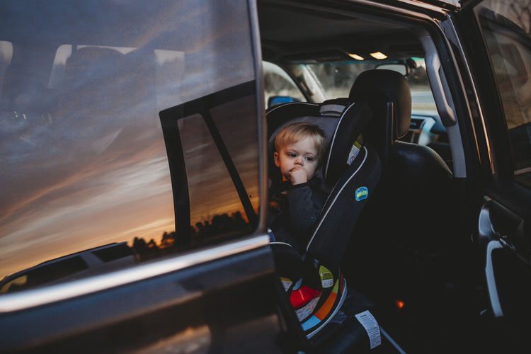 Thoughtful baby boy sitting on cat seat during sunset