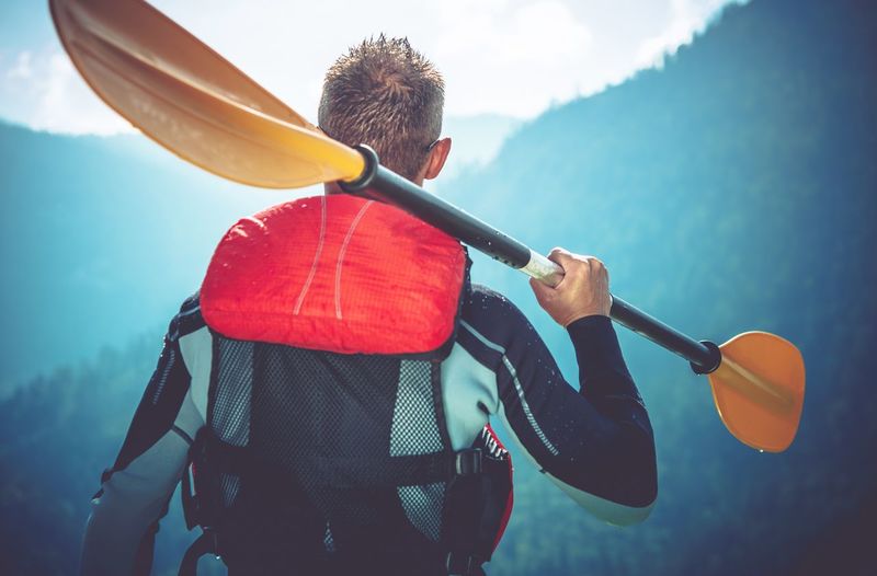 Rear view of man holding oar against mountains