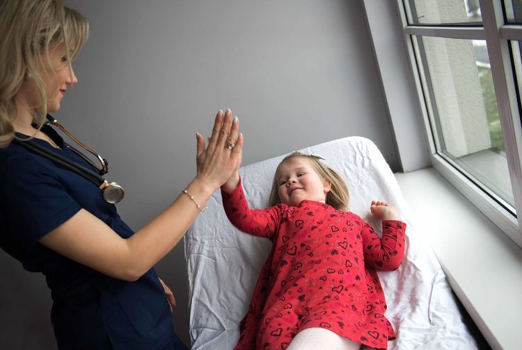 Pediatrician high-fiving with cute girl in medical clinic