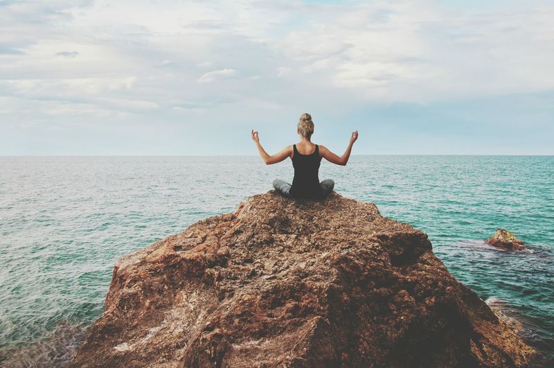Full length of woman on rock in sea against sky