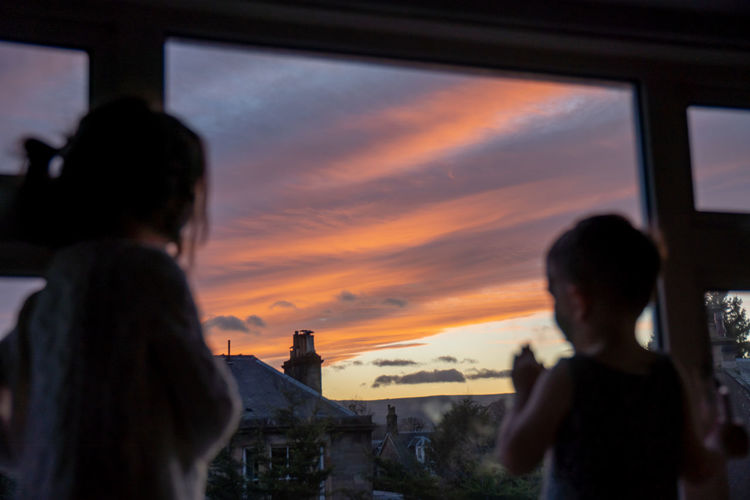 Two young children looking out of their window at a beautiful sunset view.