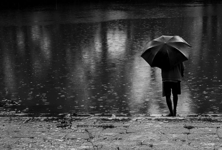Rear view of woman with umbrella walking on wet sidewalk