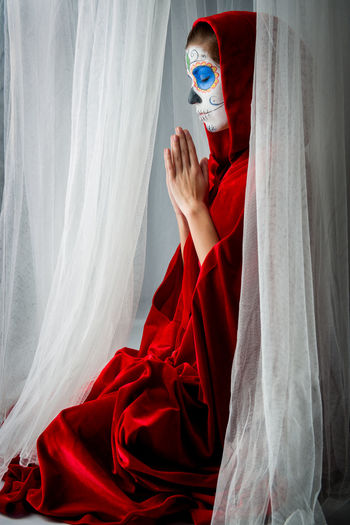 Woman with halloween make-up praying while sitting amidst curtains