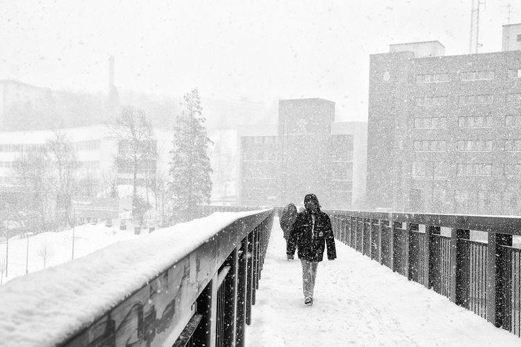 People walking on footbridge during snowfall in city
