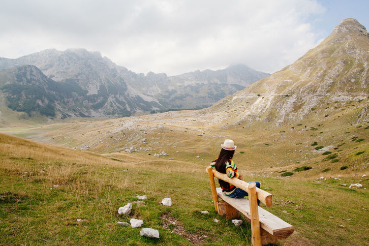 Woman sitting on bench against mountains