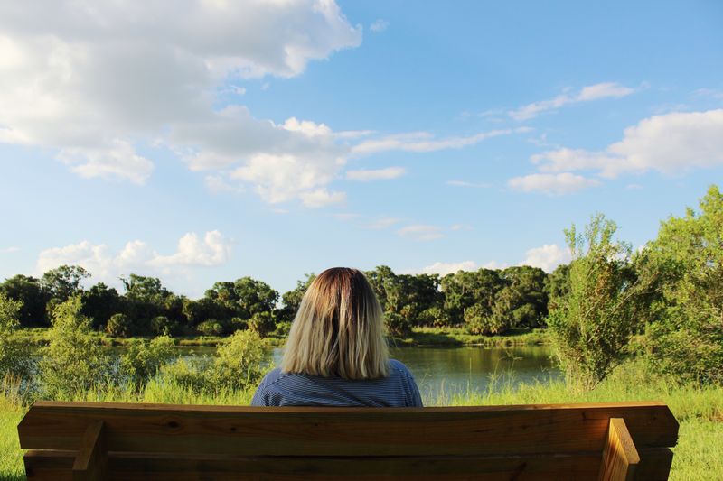 Rear view of woman sitting on bench by lake at park