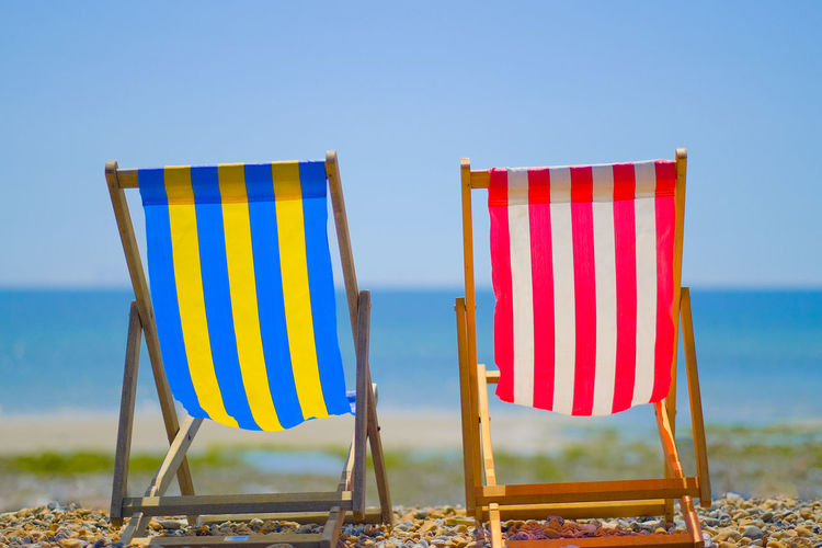 Two beach chairs sat on a stone beach against a clear blue sky