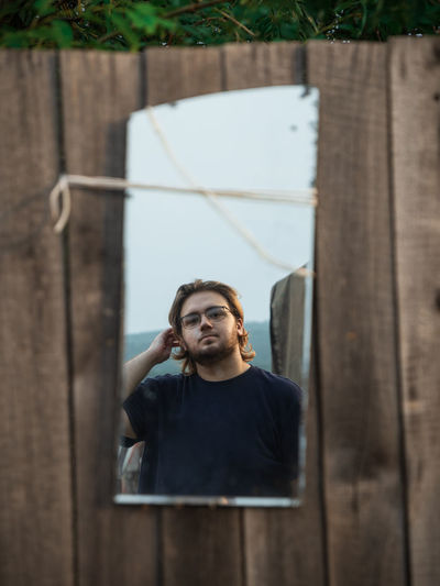 Portrait of a young man in the mirror on a wooden fence