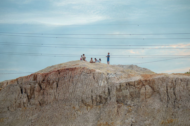 Children on rocks by mountain against sky