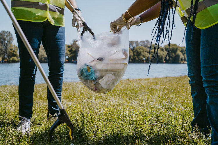 Low section of female volunteers cleaning plastics at lakeshore