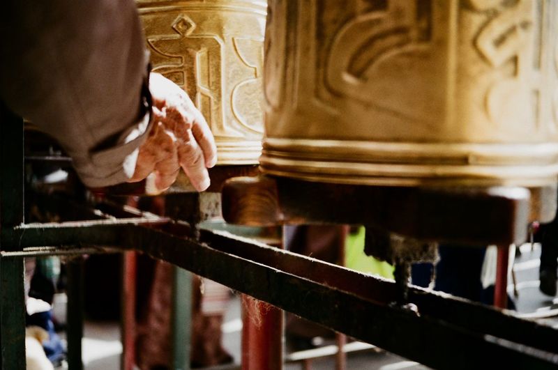 Cropped hand of man touching prayer wheels in temple